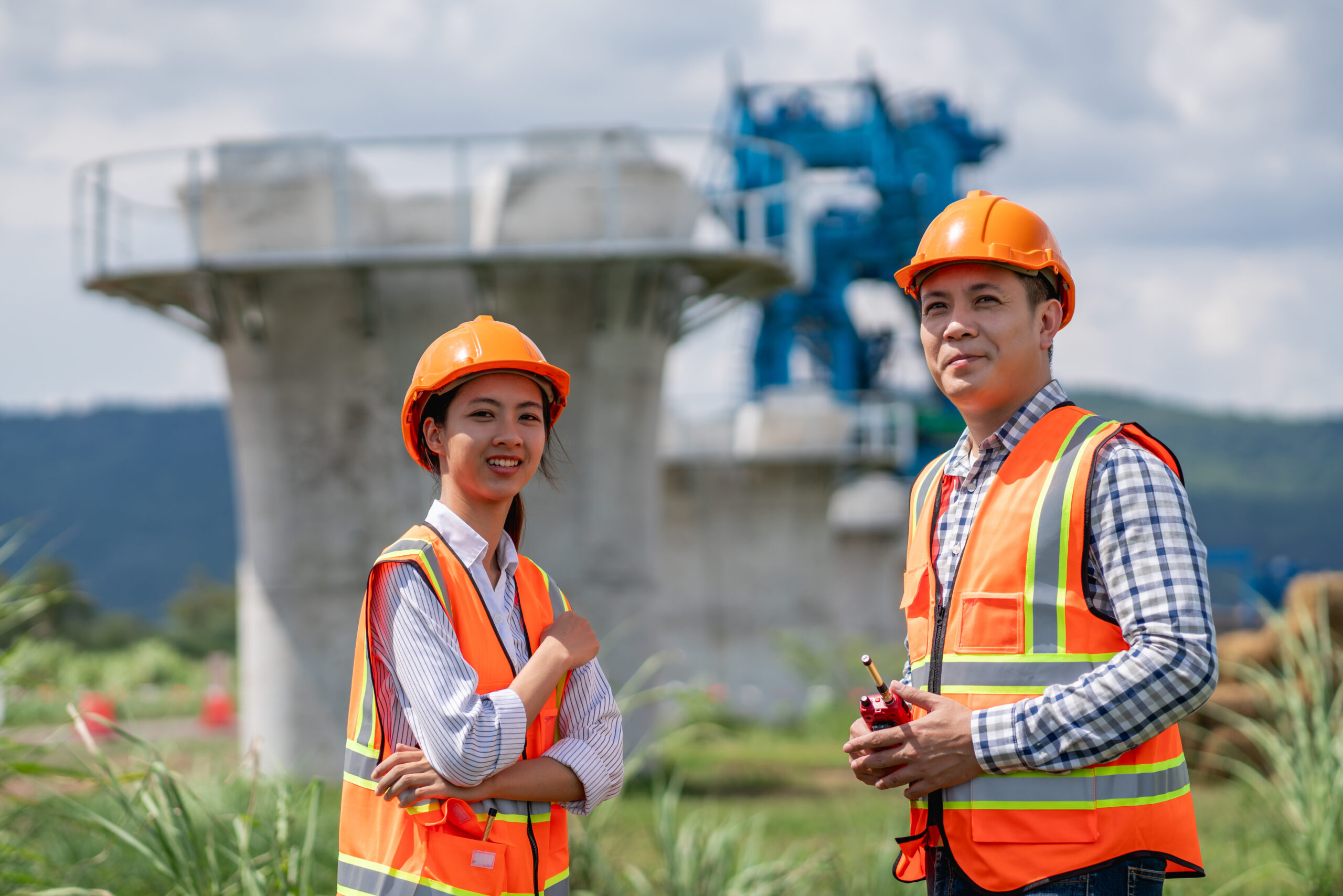 Senior construction engineer is holding paper plans and blueprints and talking with coworkers. Workers are using a survey camera at the construction site.